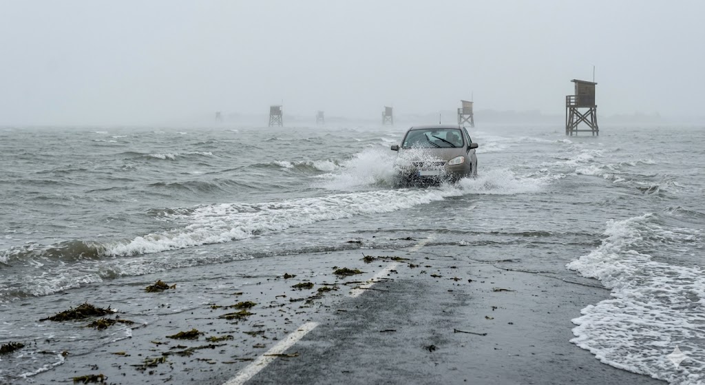 Car driving through rising ocean tides on the dangerous Passage du Gois flooded causeway in France.